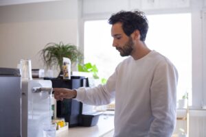 Jeune collaborateur se sert de l'eau à la fontaine à eau en entreprise