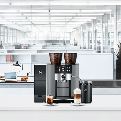 Une élégante configuration Machine à Café Location, avec moulin et mousseur à lait, est placée sur le comptoir. En arrière-plan, un bureau spacieux regorge d'éclairage lumineux, de bureaux et d'un ordinateur portable sur l'une des tables, créant un environnement idéal pour toute entreprise cherchant à combiner productivité et excellent café.